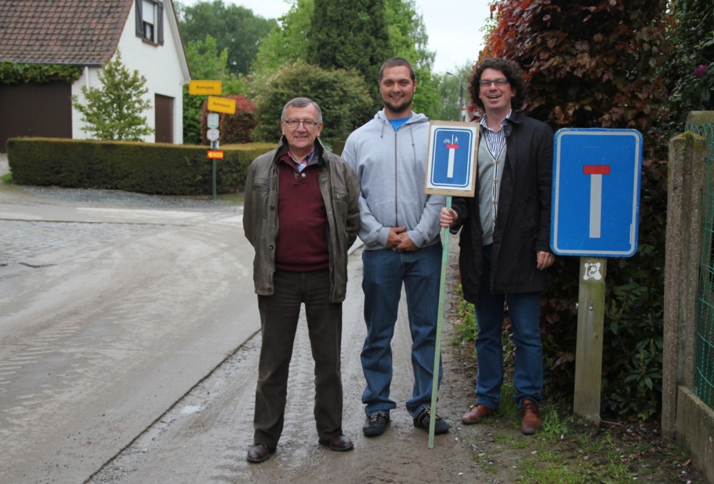 Open Vld plus-raadsleden Guy De Smet, Ruben De Gusseme en Filip Michiels aan een oud verkeersbord met voorbeeld van nieuw bord “doorlopende straat” in de hand (foto Open Vld plus)
