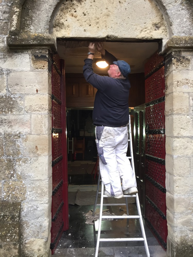Fernand De Moor herstelt het pleisterwerk boven de deuren van de kerk